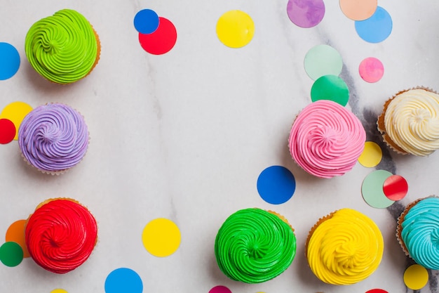 Coloridos cupcakes planos sobre el fondo de mármol con espacio para copiar. Estilo pop art con confeti de círculos de arco iris