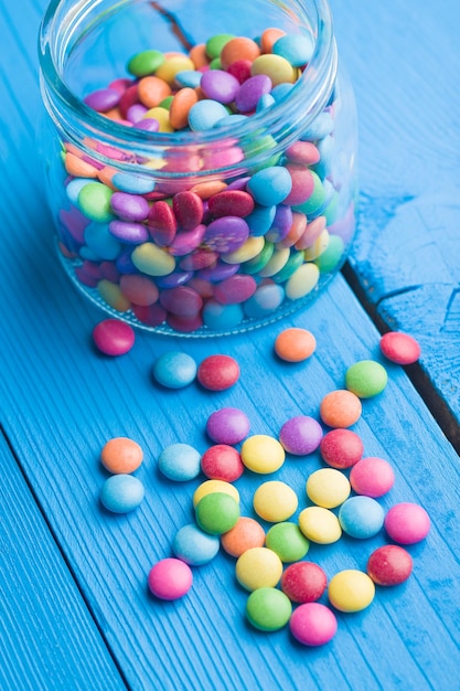Coloridos dulces de chocolate en un frasco sobre una mesa azul