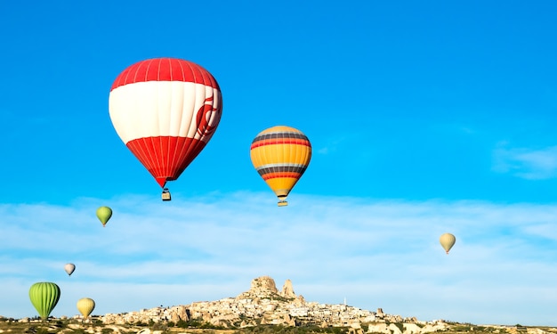 Coloridos globos aerostáticos volando cerca del castillo de Uchisar al amanecer, Capadocia