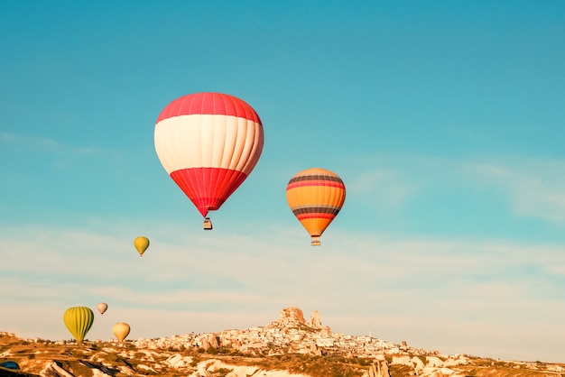 Coloridos globos de aire caliente volando cerca del castillo de Uchisar al amanecer, Capadocia, Turquía