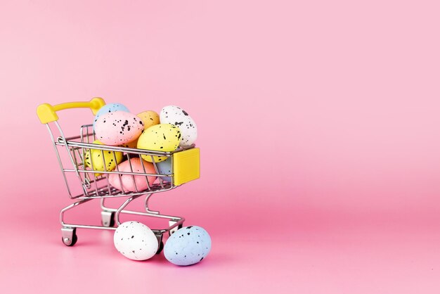 Coloridos huevos de codorniz de Pascua en carrito de compras sobre fondo rosa Copiar espacio Concepto mínimo de Pascua