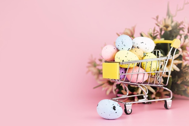 Coloridos huevos de codorniz de Pascua en carrito de compras sobre fondo rosa Copiar espacio Concepto mínimo de Pascua
