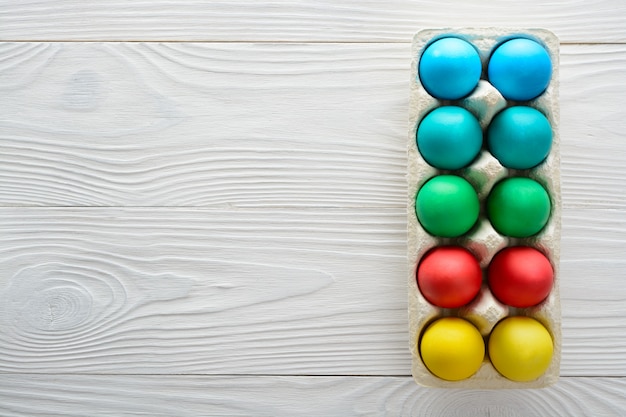 Coloridos huevos de pascua en una bandeja sobre una mesa de madera blanca