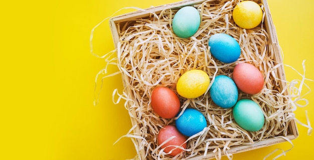 Coloridos huevos de Pascua en canasta sobre fondo amarillo Familia con niños preparándose para Pascua en casa