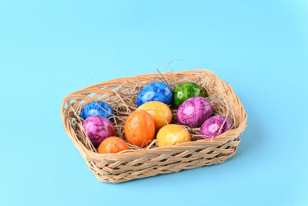 Coloridos huevos de pascua en la canasta sobre el fondo azul.