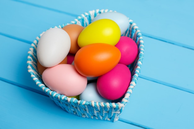 Coloridos huevos de pascua en la cesta aislada en una pared azul