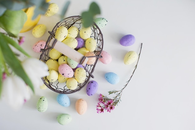 Coloridos huevos de Pascua en cesta de metal vintage y flores sobre un fondo blanco.