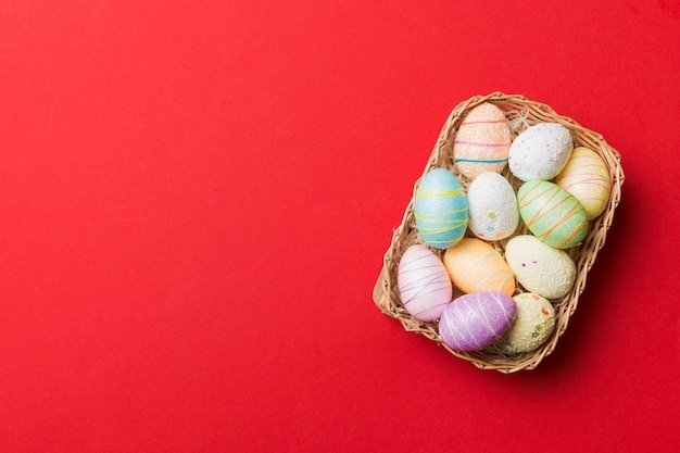 Coloridos huevos de Pascua en cesta de mimbre contra el fondo de color closeup vista superior con espacio de copia