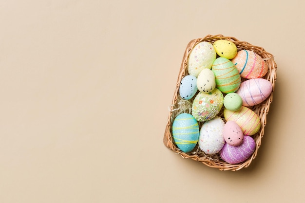 Coloridos huevos de Pascua en cesta de mimbre contra el fondo de color closeup vista superior con espacio de copia