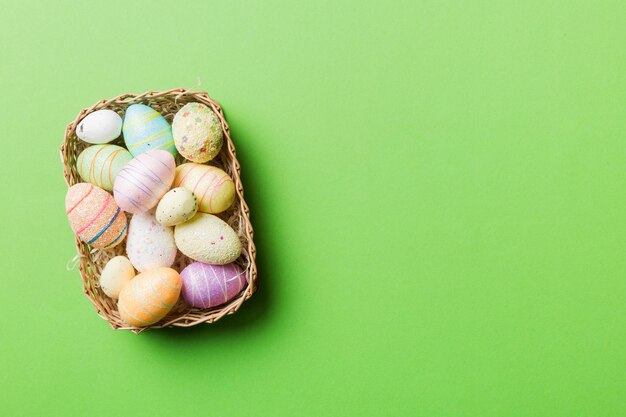 Coloridos huevos de Pascua en cesta de mimbre contra el fondo de color closeup vista superior con espacio de copia