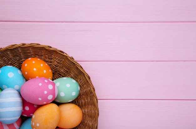 Coloridos huevos de pascua en la cesta sobre fondo de madera rosa