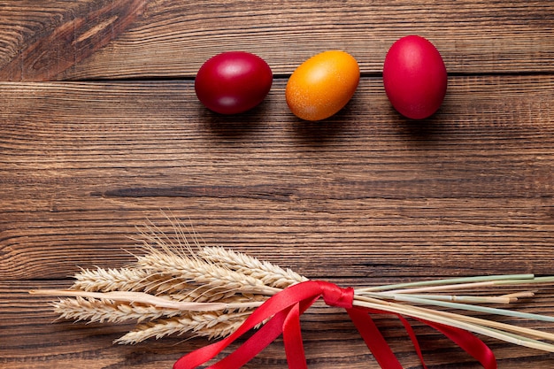 Coloridos huevos de Pascua con espigas de trigo sobre fondo de madera marrón