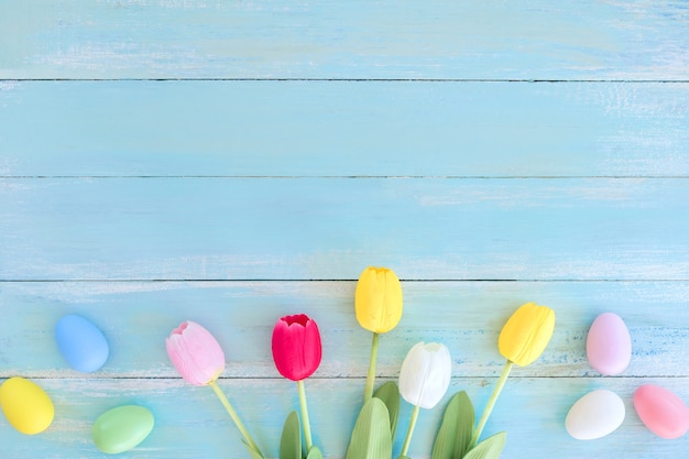 Coloridos huevos de Pascua con flores de tulipán en el fondo de madera azul