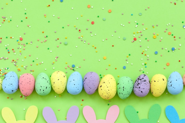 Foto coloridos huevos de pascua y guirnalda de pascua de conejito hecho a mano sobre fondo verde. vista superior, endecha plana. concepto de pascua feliz.