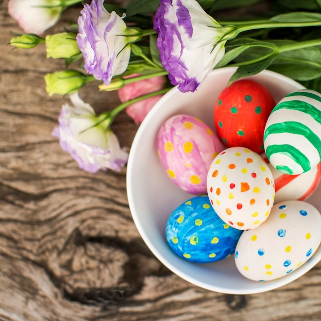 Coloridos huevos de pascua y lisianthus en mesa de madera