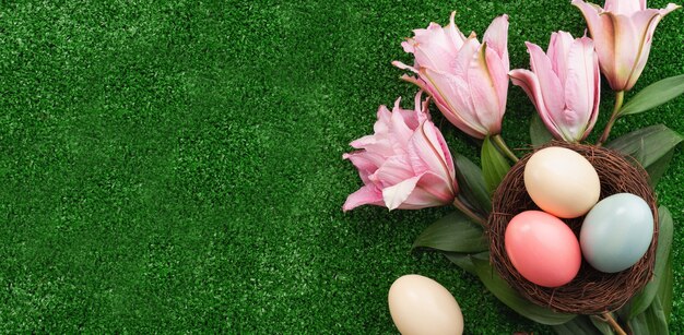 Coloridos huevos de Pascua en el nido con flor de lirio rosa sobre una superficie de césped.