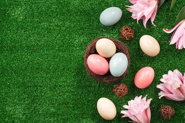 Coloridos huevos de Pascua en el nido con flor de lirio rosa sobre una superficie de césped.