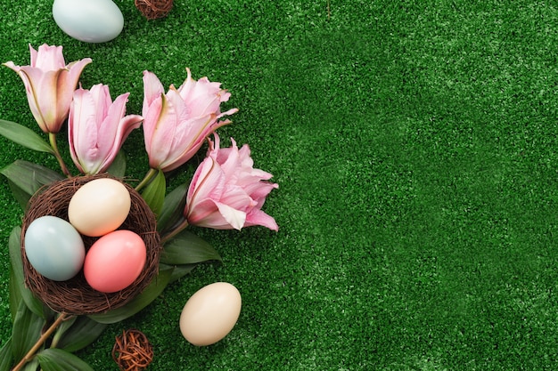 Coloridos huevos de Pascua en el nido con flor de lirio rosa sobre una superficie de césped.