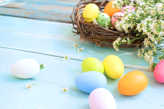 Coloridos huevos de Pascua en el nido con flores sobre fondo azul de madera