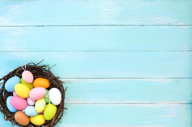 Coloridos huevos de Pascua en el nido en el fondo de madera azul.