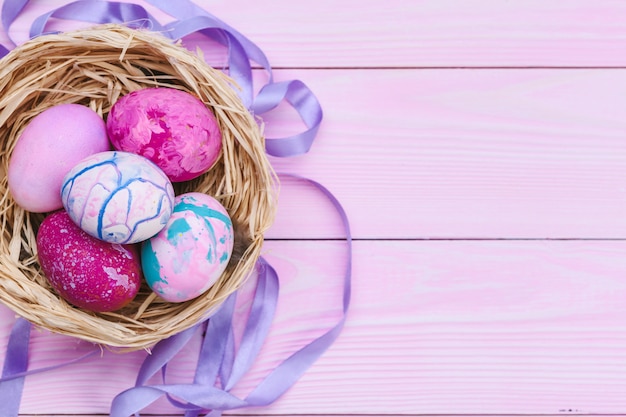 Coloridos huevos de pascua en un nido sobre fondo de madera rosa