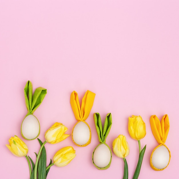 Coloridos huevos de Pascua con orejas de tela como conejito de Pascua. La primavera verde y amarilla brillante florece el tulipán en rosa con el espacio de la copia. Concepto de vacaciones de primavera.
