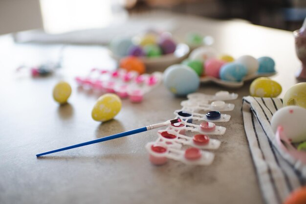 Coloridos huevos de Pascua con pincel y pinturas en la mesa de la cocina de cerca