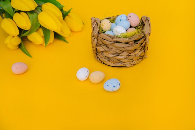 Coloridos huevos de pascua pintados en canasta con flores de tulipán amarillo