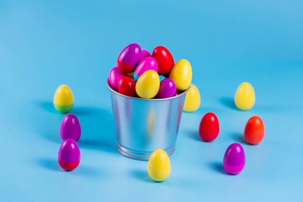 Coloridos huevos de Pascua de plástico en un cubo de metal sobre fondo azul.