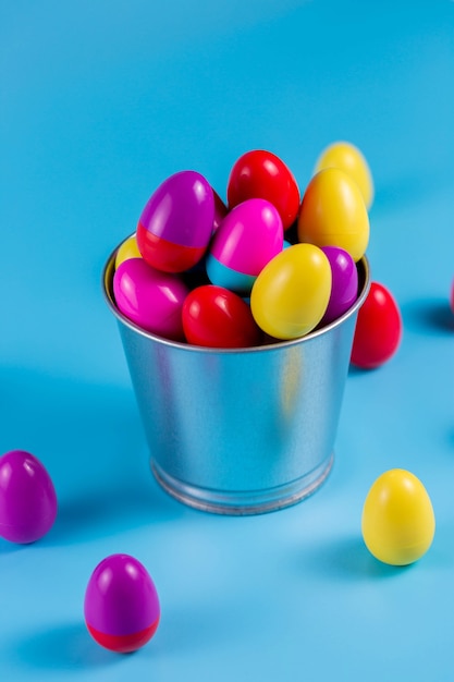 Coloridos huevos de Pascua de plástico en un cubo de metal sobre fondo azul.