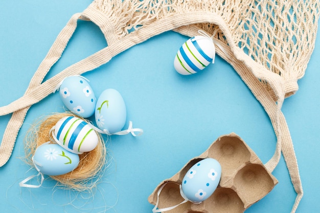 Coloridos huevos pintados de pascua y bolsa de hilo de algodón sobre fondo azul.