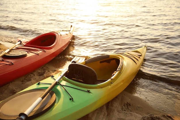 Coloridos kayaks con remos cerca del agua en la playa del río al atardecer Actividad de campamento de verano