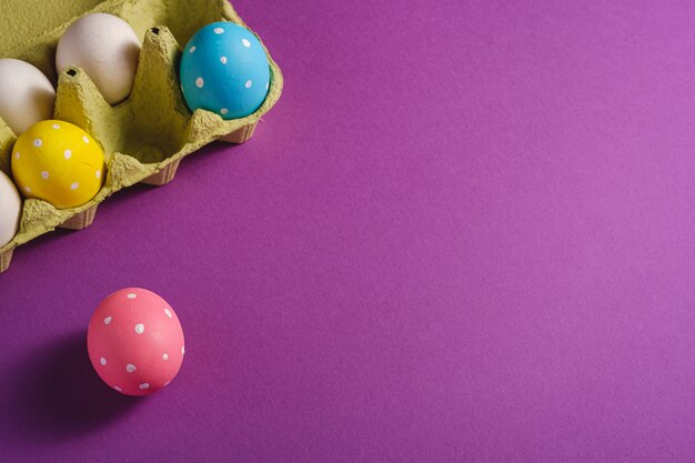 Coloridos lunares huevos de Pascua en bandeja de huevos sobre fondo liso violeta púrpura, tarjeta de felicitación, espacio de copia, ángulo de visión