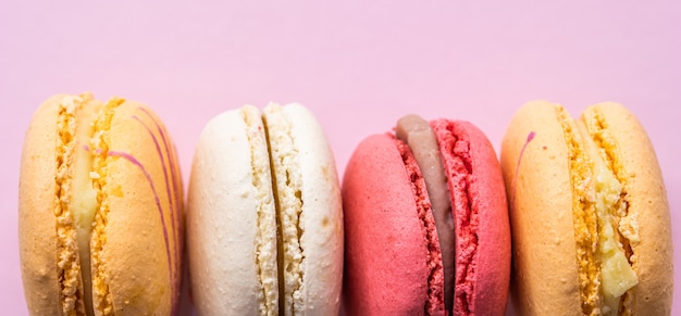 Coloridos macarons de galletas francesas en fondo rosa pastel de galletas dulces de almendra fruta sabrosa