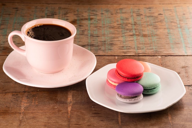 Coloridos macarons rellenos de chocolate en un plato de cerámica blanca sobre una mesa rústica de madera con una taza de café caliente