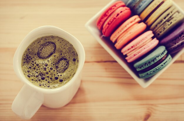 Coloridos macarrones y té verde en mesa de madera