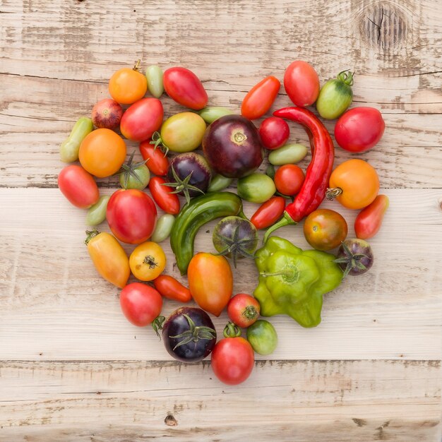 Coloridos vegetales orgánicos tomates y pimentón en forma de corazón sobre fondo de madera