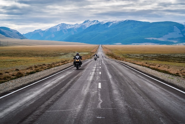 Columna de motocicletas viajando a lo largo del tracto Chuysky al amanecer, paisaje con una carretera. Rusia, montaña Altai