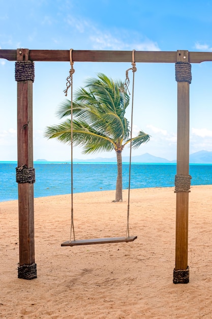 Columpiarse en una playa de arena con vistas a la palmera azul del mar y al cielo El concepto de descanso y relajación