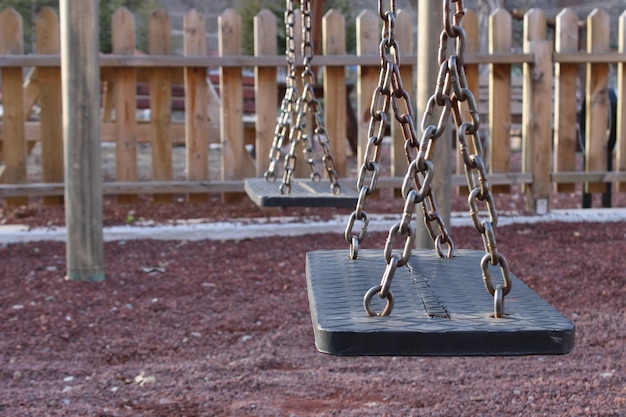 Un columpio con cadenas y una valla al fondo.