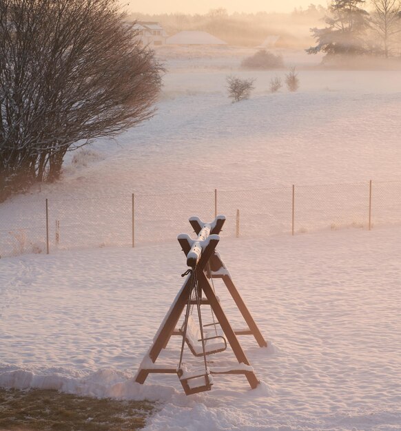 Columpio cubierto de nieve de madera durante un atardecer de invierno