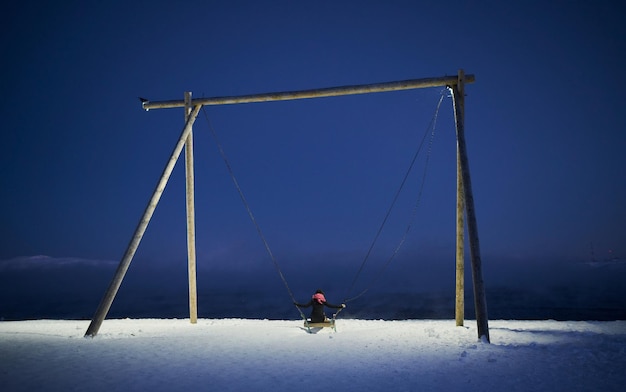 Columpio de juegos con nieve espesa en el suelo y vistas a la montaña y al cielo nublado