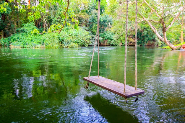 Columpio de madera en el río en el bosque