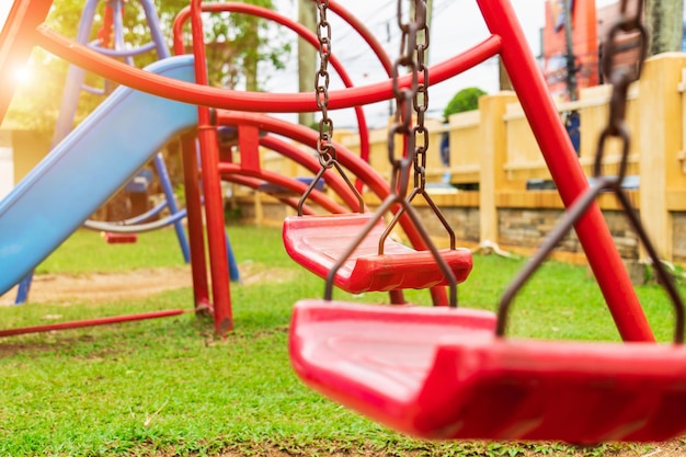 Un columpio rojo está unido a dos viejas cadenas oxidadas en el patio de recreo del parque vio el suelo y la hierba