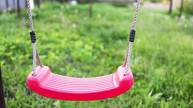 Un columpio rojo vacío y solitario cuelga en un jardín lleno de árboles en flor y pasto verde en una cálida primavera.