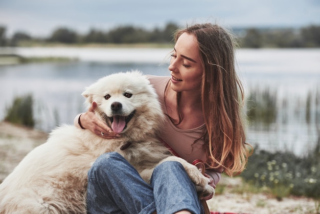 Com a língua de fora. está quente lá. a menina loira com seu lindo cachorro branco passa um grande momento na praia.