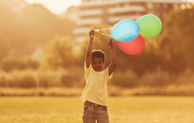 Com balões nas mãos, criança afro-americana se diverte no campo no dia de verão