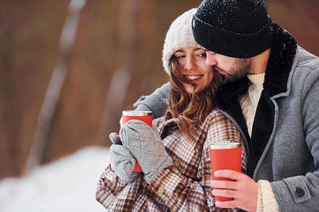 Com bebida casal alegre passear na floresta de inverno durante o dia