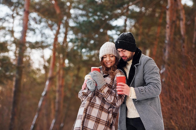 Com bebida Casal alegre passear na floresta de inverno durante o dia