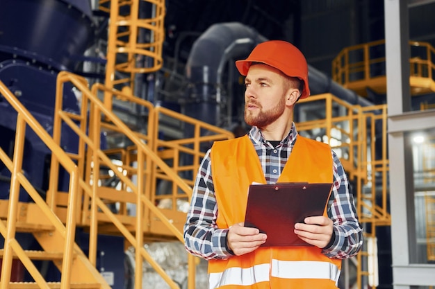 Com bloco de notas Trabalhador da construção civil de uniforme está na fábrica